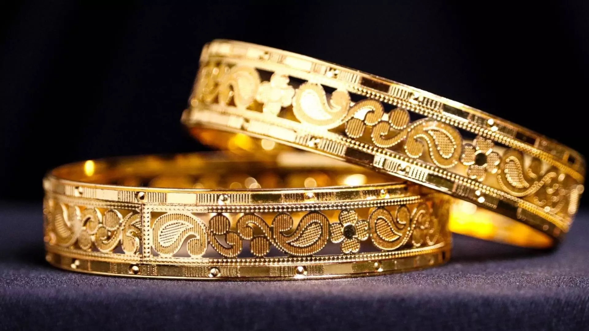 two gold bangles in an indian design with black background