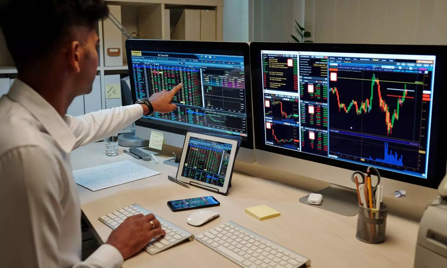 a man sitting in front of computer screens which showing stock market trends